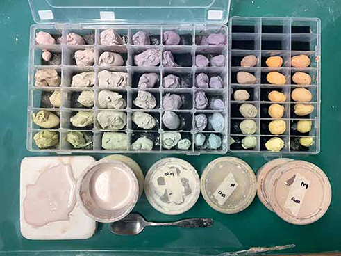 1 At the top of the image are two foam-lined bead-organizer boxes holding the colored-clay gradients in plastic-clay form. The bottom left of the image shows a small plaster slab used to dry out slip to the plastic-clay state, and the small round containers hold colored clay in slip form. 