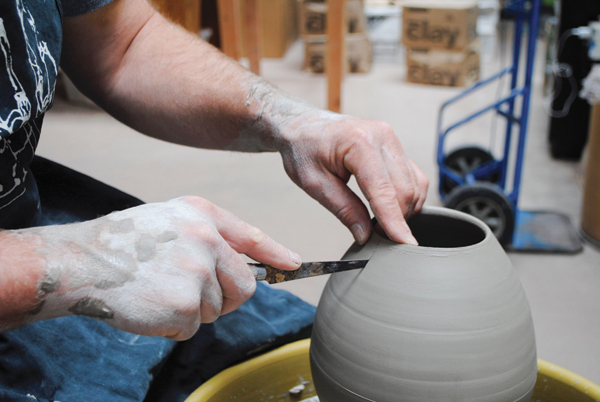 4 Cut out a section of the pitcher body, starting at the rim and drawing the fettling knife straight down to the line marked around the circumference of the pot. This cut starts to alter the symmetrical shape.