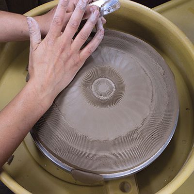 4 Use the side of your palm to begin forming the coil into a foot. Use a 12-teeth-per-inch serrated metal rib to gently move the clay around, compressing the coil into the slab and making a seamless joint. 