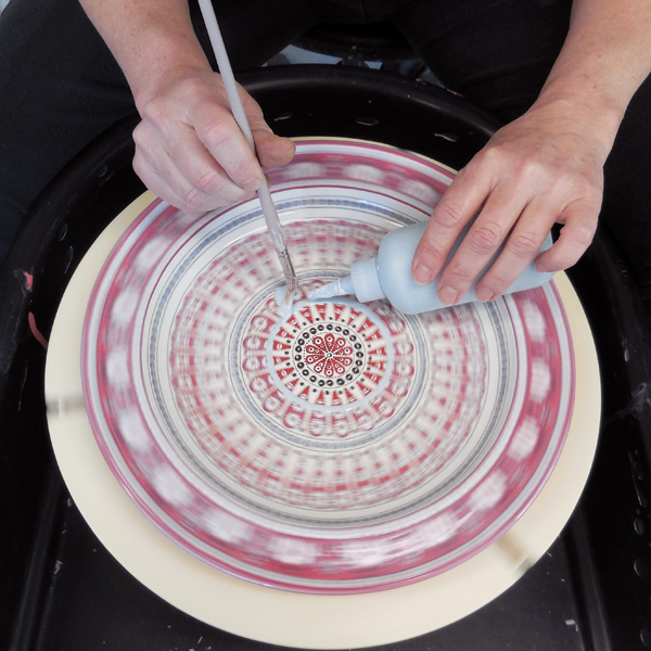 10 Applying glaze to the bisque-fired platter with a brush and squeeze bottle while slowly rotating the plate on the wheel.This method ensures a more even coat of glaze.