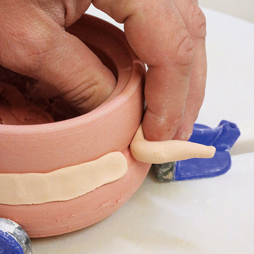 3 Press a coil of colored clay into an incised line, creating a band of inlay. 
