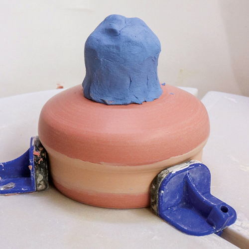 4 Attach a golf-ball-sized piece of clay onto the trimmed base to throw into a foot. 
