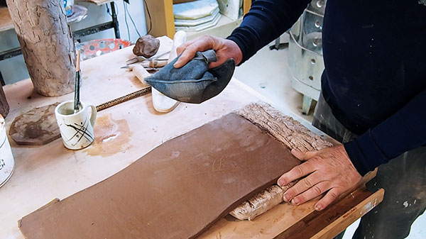 3 Ingersoll applying texture to a clay slab using a sandbag and bisque-fired texture slab.