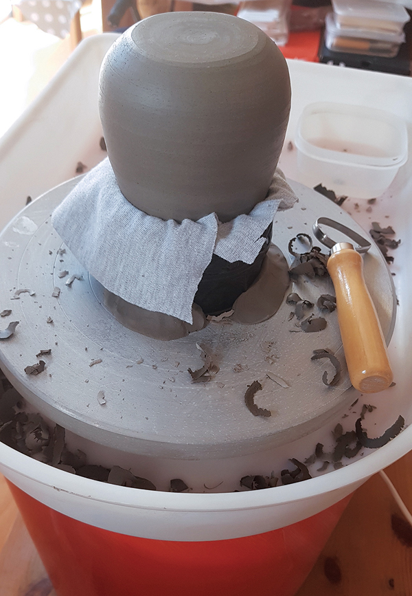 3 Center the chuck on the wheel and secure it in place with clay lugs. Place the vase into the opening and make sure it is level and secure prior to trimming.  