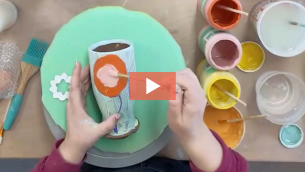 Image of Amy Irish painting brightly colored underglazes onto a wheel-thrown tumbler.
