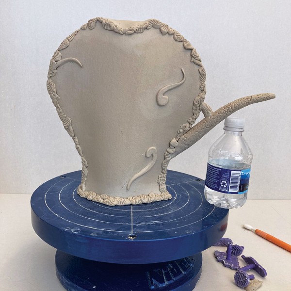 7 Attach the spout using supports. Add thin clay applique pieces to the surface.
