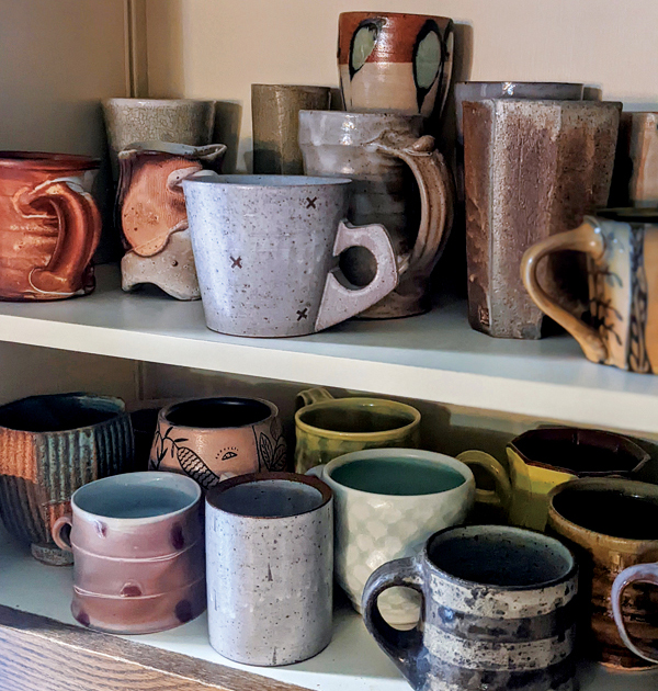 5 Interior view of a cupboard showing a collection of regularly used cups and mugs, by various artists.