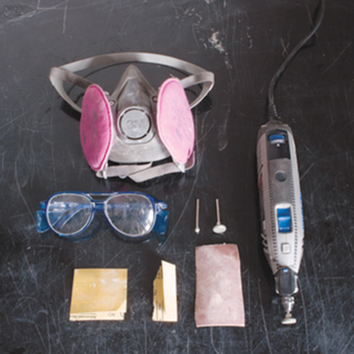 1 Tools for cleaning up fired works. Clockwise from top left: respirator, grinding bits for a rotary tool, rotary tool, cut section of a belt-sander belt, sandpaper, and safety glasses. 