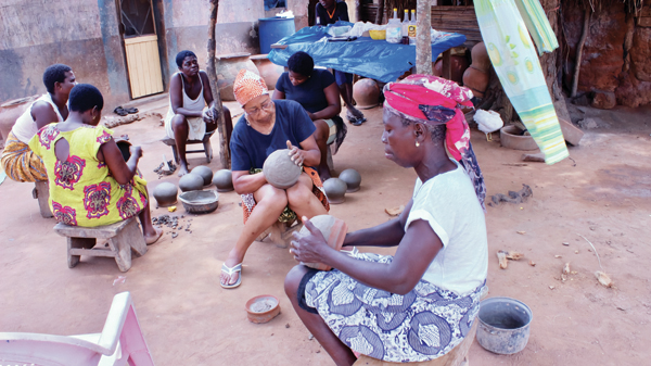 3 Winnie Owens-Hart (center) apprenticing under Peace (right) in Kuli Pottery Village, working on a traditional pot.