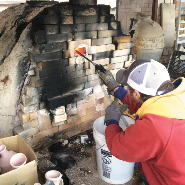 3 Justin Rothshank spraying soda into the wood kiln using a soda blaster, which consists of a hose pulling soda solution out of a 5-gallon bucket, powered by an air compressor. 