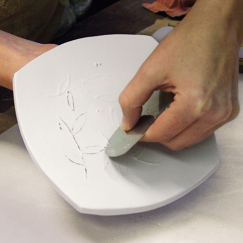 5 Apply 1–2 coats of underglaze. After it dries, use a metal rib to gently scrape the raised lines to expose the red clay below.