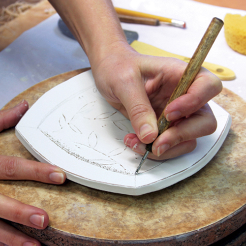 6 Carve lines using a sharp-pointed tool. Create a frame around the surface decoration echoing the plate shape.