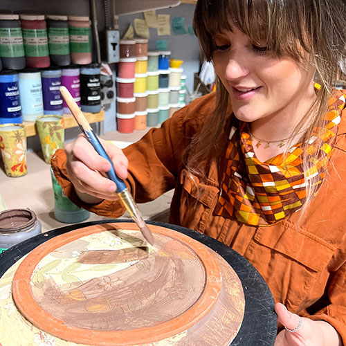 Lakyn Bowman paints an underglaze wash on a plate.