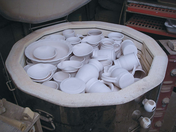 7 Tumble-stacked top-loading kiln with pie plates, spoon rests, vase, and mugs placed on top layers.