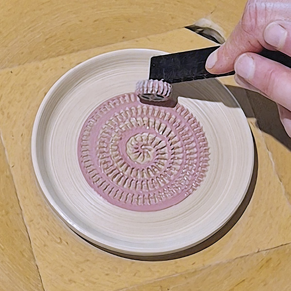 3 Hold the tool in the center of your freshly thrown dish and slowly move it with light pressure from the center to the outside while spinning your wheel slowly.