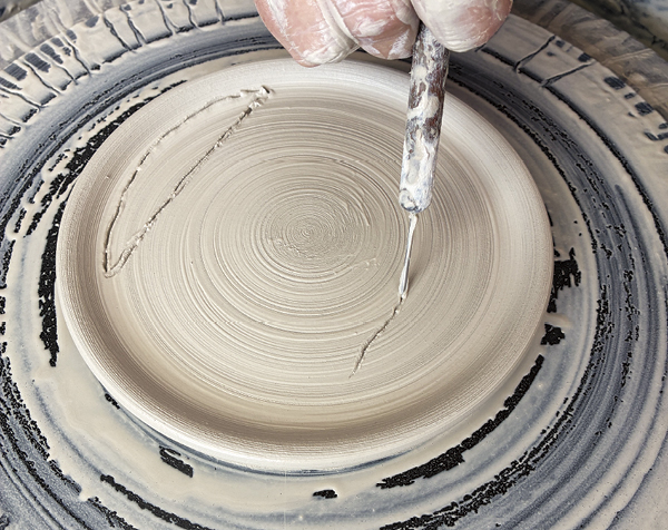 2 Use a needle tool to cut mirrored crescent-shaped darts on each side of the dish all the way to the wheel head.