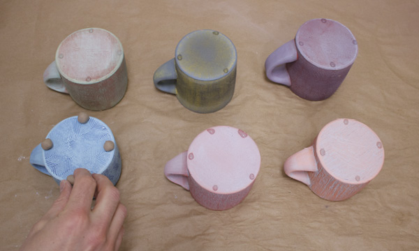 2 Neil Celani preparing mugs for firing. Glue is used to hold wads onto mugs.