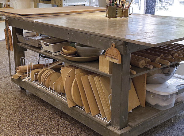 A carefully designed work bench features a variety of storage options beneath the work surface including open drawers and vertical organizers.