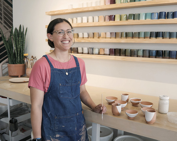 2 Clay educator, Olivia Tarricone, in front of HTX Clay’s glaze test-tile wall.