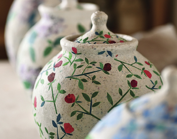 9 A series of biodegradable urns drying on a studio worktable. The urns are wheel-thrown, using reclaimed porcelain and cellulose fibers, with surfaces decorated with hand-painted details and soy-based paper cutouts. Because the urns are unfired they will degrade naturally.