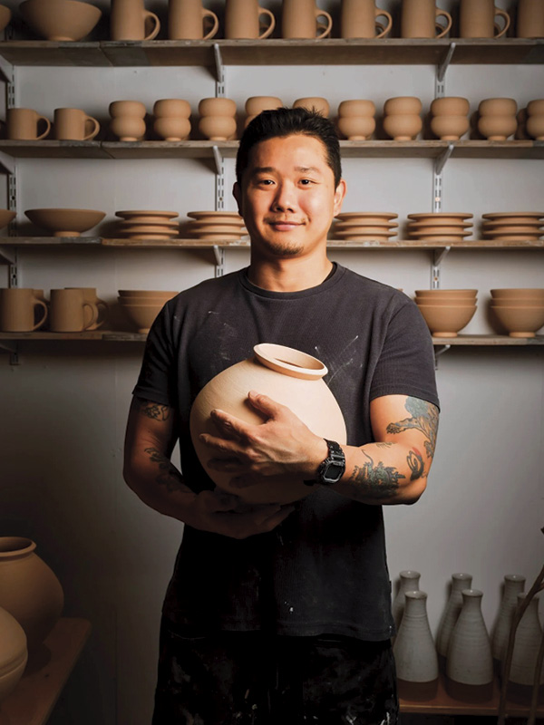 1 Jun Rhee in his studio, holding a Moon Jar in front of bisque-fired vessels. Photo: Jonathan Page.