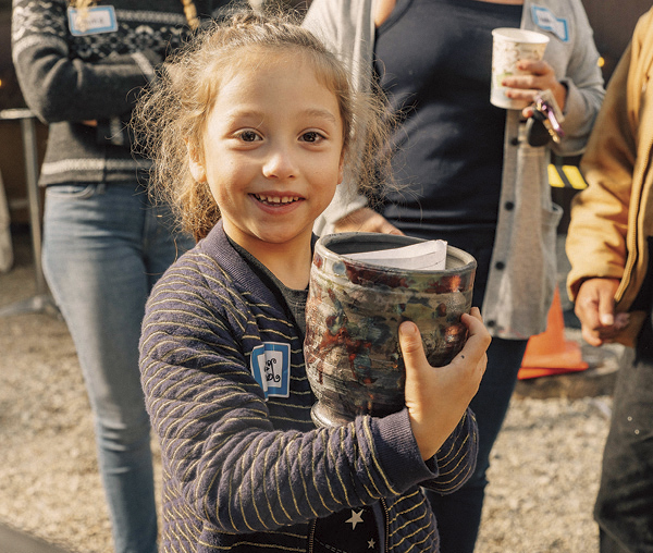 3 A young participant proudly displays her finished pot during Pewabic’s annual Raku Party. Photo: Aaron Barton.