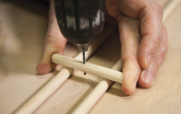 4 Drill holes through the center of both dowel handles. If you don’t feel comfortable drilling as shown, use a vise.