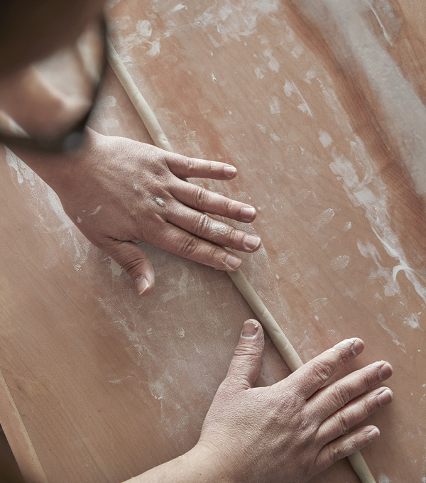 Hands rolling clay on a wood work table.