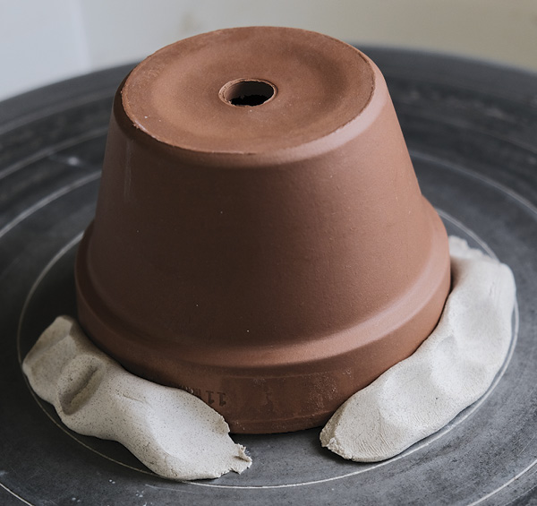 1 Place the flower pot upside down on your wheelhead, center, and secure with coils of moist clay.