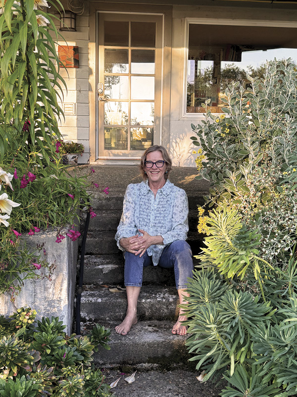 1 Liz Quackenbush in the garden outside her West Seattle studio, 2026. Photo: Erin Shafkind.