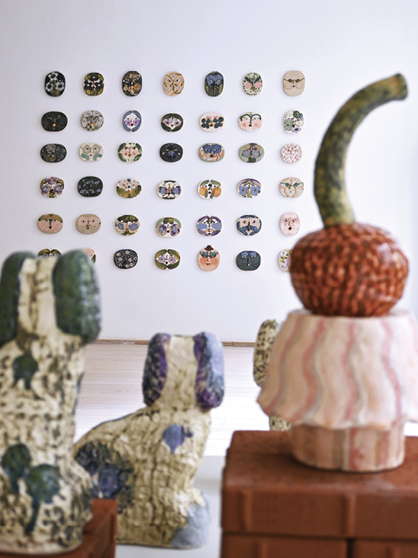 6 Installation view of “Off Duty” exhibition; background: face reliefs; foreground: collection of dog sculptures and the cake sculpture, Cherry Temptation, stoneware, glazes, 2023–2024.