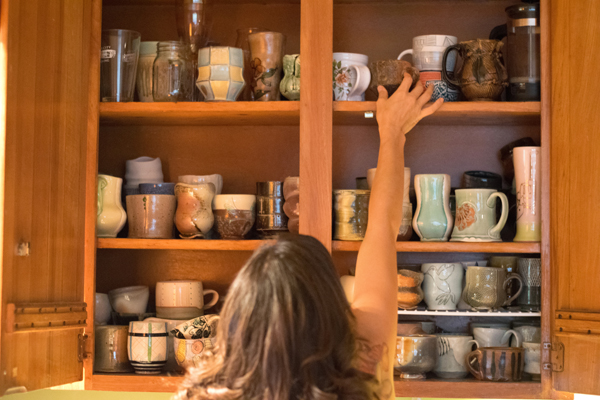 2 Makenzie Schiemann selecting a mug from the kitchen cabinets. 