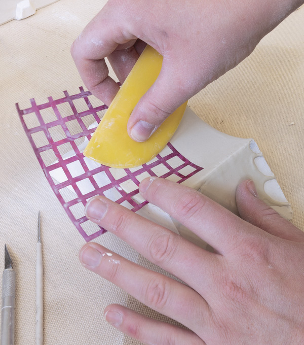 1 Coat the mold in white casting slip. Use a soft rubber rib to press a vinyl template into the surface, transferring the pattern.