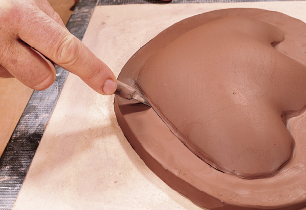 4 Place pieces on a board. Press along the flat slab to articulate edges. At medium leather hard, make a 45° cut around shapes.