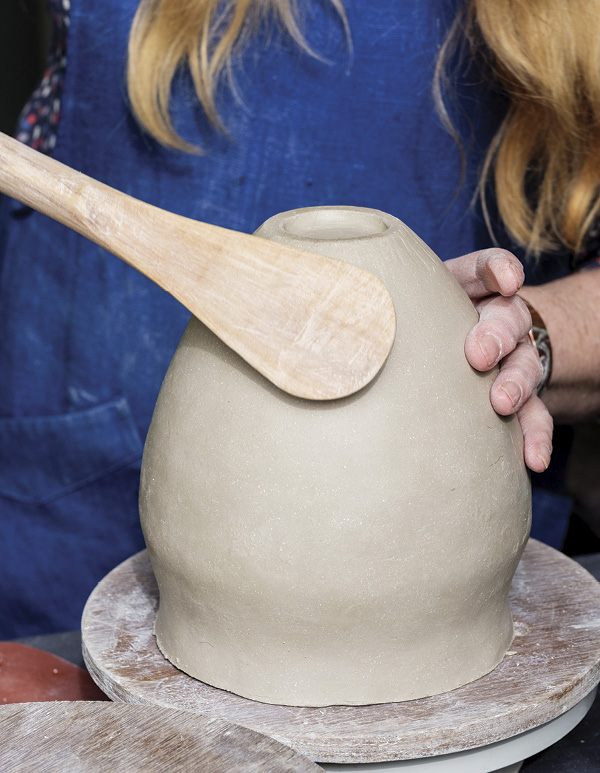 3 Use a flat spoon to beat the clay and develop a narrower base.