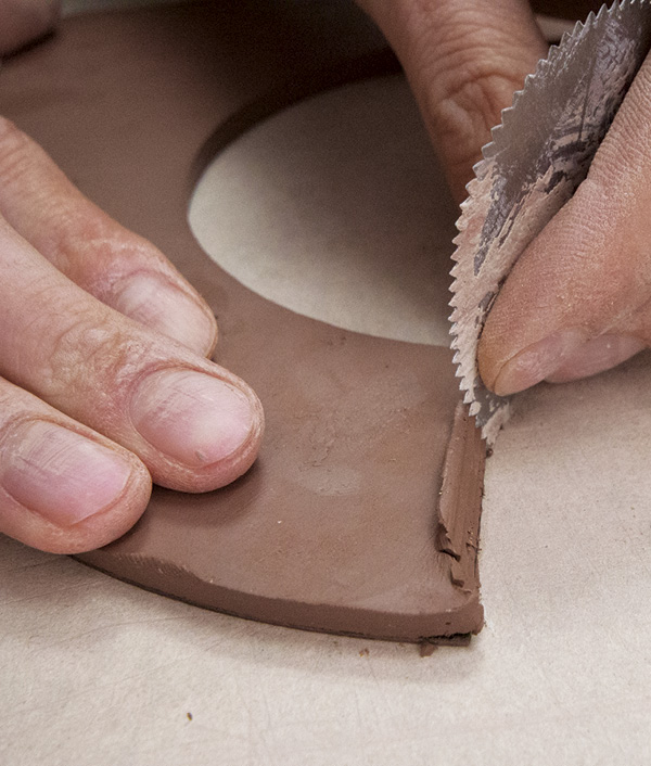 5 Scrape a serrated rib along the joining edges to create a lip of clay, then add score marks.