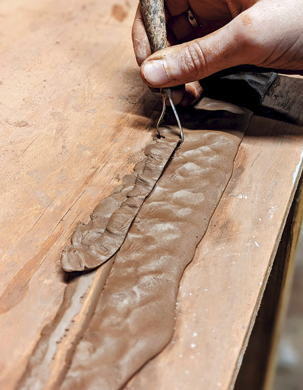 7 Use a ribbon tool to cut a long, thin strip of clay from a flattened coil.