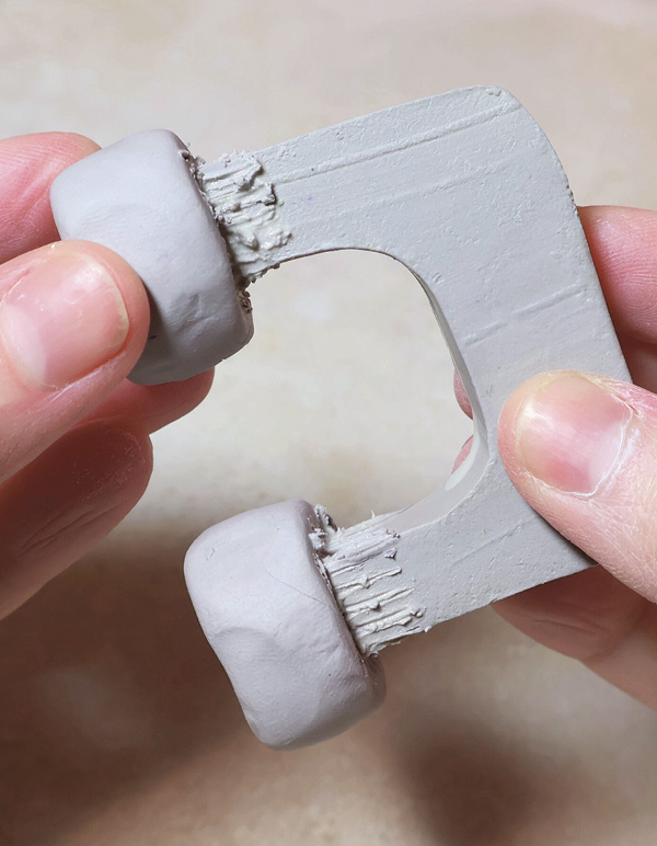 9 Add small balls of clay to each end of the handle. Smooth them into the form.