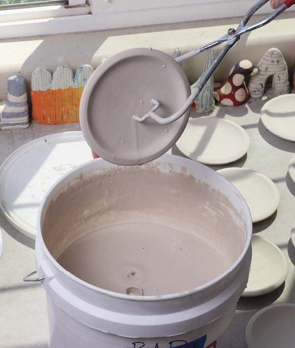 6 Sand the bisqueware to smooth out the foot ring, then dip the dish into a bucket of glaze.