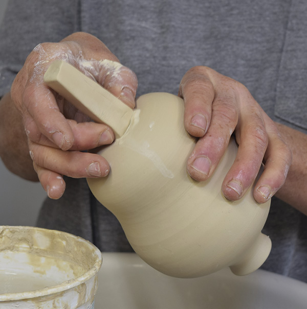 6 Create a handle slug about 1½ in. (3.8 cm) long by rolling a coil and flattening it. Scrub the bottom of the feeder with Magic Water to make slip and press the handle slug into the slip. Sponge around it to remove excess slip and attach it securely.