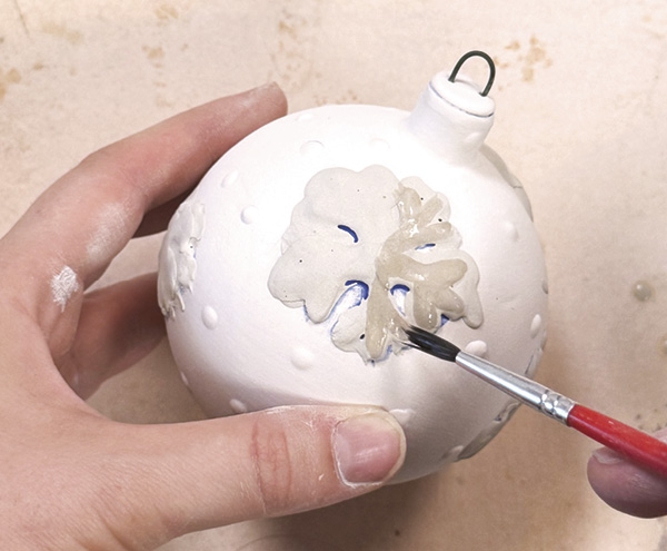 7 Apply clear glaze over the snowflake, then brush wax over to protect color. Finally, cover ornament in transparent blue glaze.