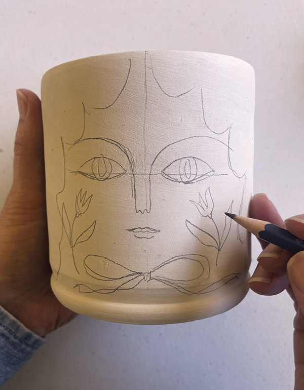 5 Lightly pencil sketch faces and hair onto the greenware mug shape.
