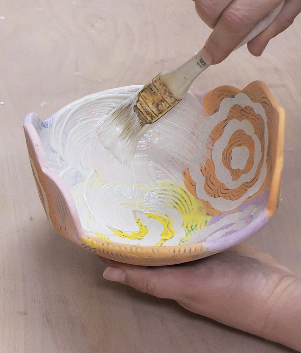 13 Brush white slip over the bowl, covering all the paper pieces. Three coats is generally enough to create contrast.
