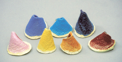 Test glazes, each consisting of 8 parts Sumi's Volumetric Clear to 1 part Mason stain. Back row, left to right: stain 6319 (Lavender), 6364 (Turquoise) and 6387 (Mulberry). Front row, left to right: stain 6000 (Shell Pink), 6407 (Marigold), 6121 (Saturn Orange) and 6006 (Deep Crimson). Tests are on cones made from slabs rolled out on lace to show how the glaze looks on a textured surface.