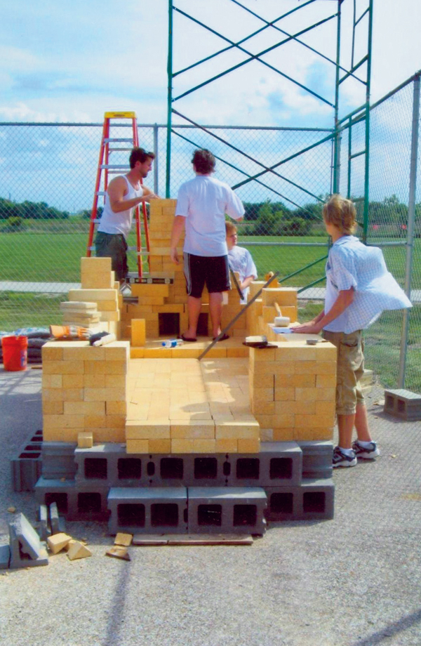 Two layers of concrete block form the foundation and raise the kiln to a workable height. Students build the walls and begin the stack.