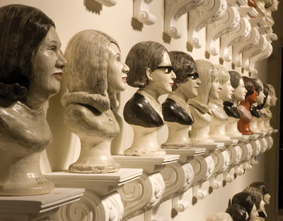 Detail view of the large wall of portraits in a grid-like arrangement. The name of the individual portrayed is stamped on the base of each portrait bust.