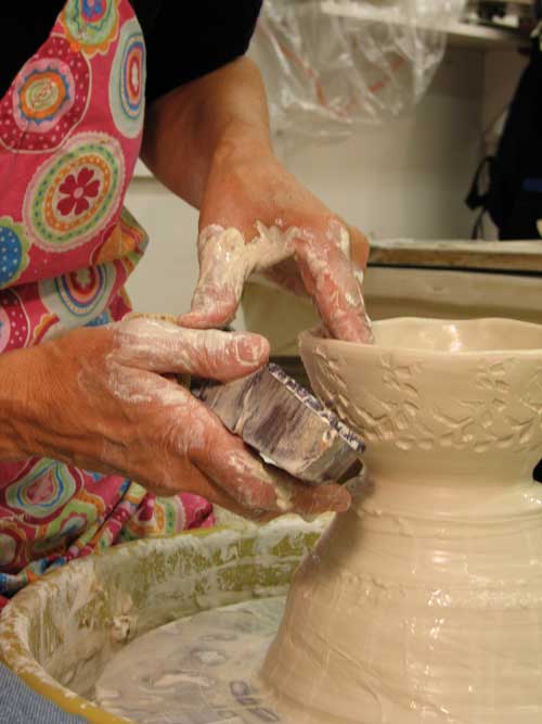 Wooden textile-printing blocks are wetted to prevent them from sticking to the clay. They are pressed into the surface while the form, thrown slightly thicker than normal so it can stand up to the stamping, is supported from the inside.