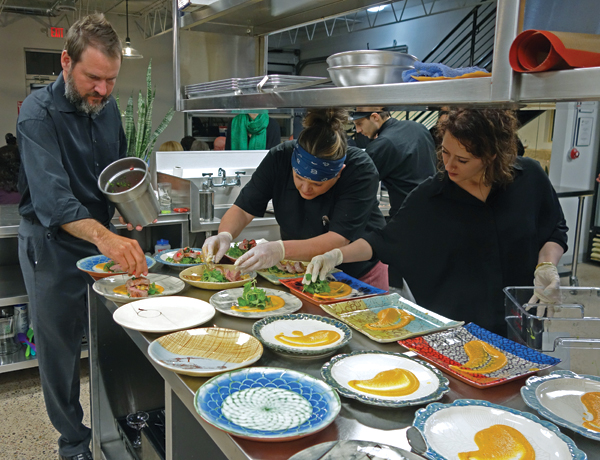 3 Farmer Ric Murphy, Chef Carrie Eagle, and Sarah Schoen plating the main course on pottery by Maggie Beyeler, Jen DePaolo, Lauren Karle, and Betsy Williams, to 10 in. (25 cm) in diameter, mixed ceramic, 2017. Cuisine by Chef Carrie Eagle of Farm and Table Restaurant.
