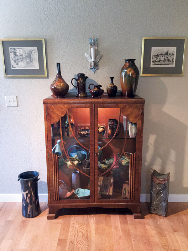8 An Art Deco cabinet filled with American art pottery, a wall pocket by David Keyes above the cabinet in the center, and two early Sam Scott pieces on each side of the cabinet.