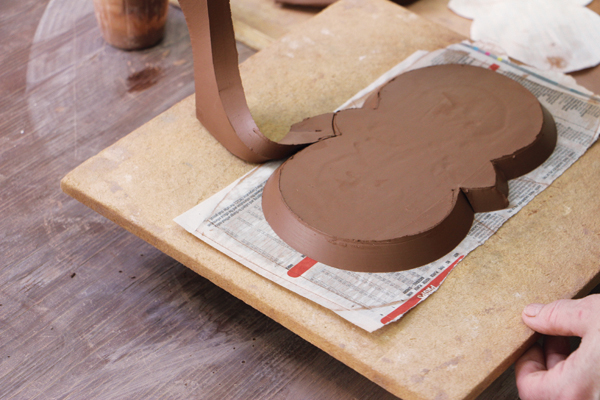 4 Remove the extra clay and use a rib to compress the angled edge. Place a board on top and flip the base over.